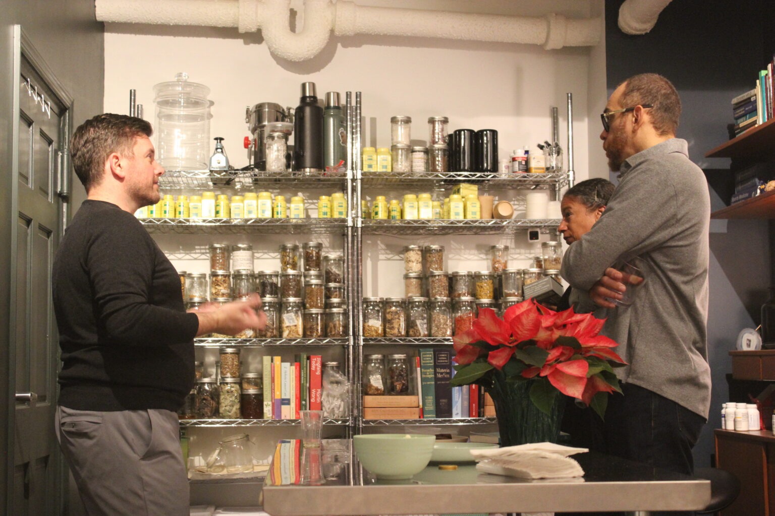 Dr. Caron talking with two colleagues in front of shelves of Chinese herbs