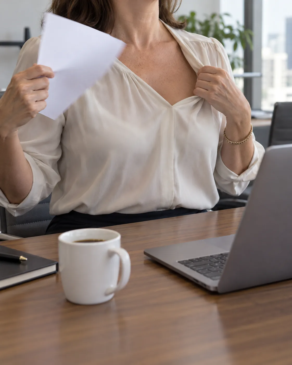 Woman at an office desk fanning herself with a sheet of paper during a hot flash